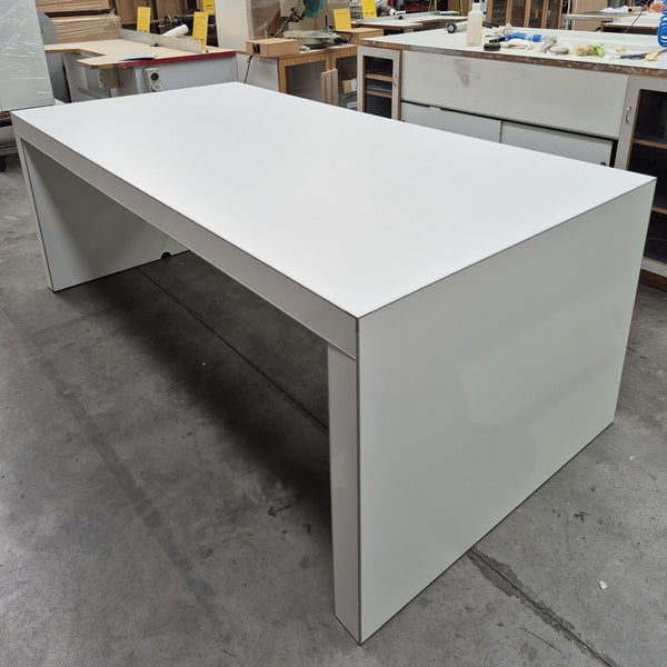 A modern white rectangular electronics retail display table desk  photographed in a warehouse setting.