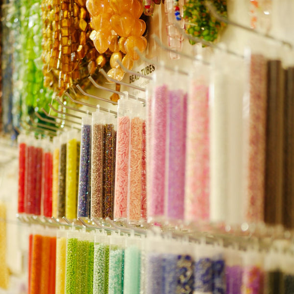 A close-up view of a display wall filled with many clear plastic tubes containing colorful craft beads or sprinkles in pink, purple, blue, green, orange, and brown tones  hung on slatwall with Plankwall light duty single prongs.