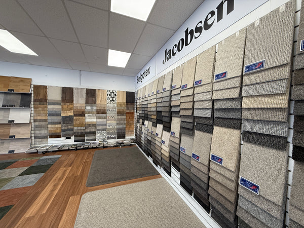 Display of carpet samples in a showroom mounted on white slatwall panels with 'Jacobsen' branding.