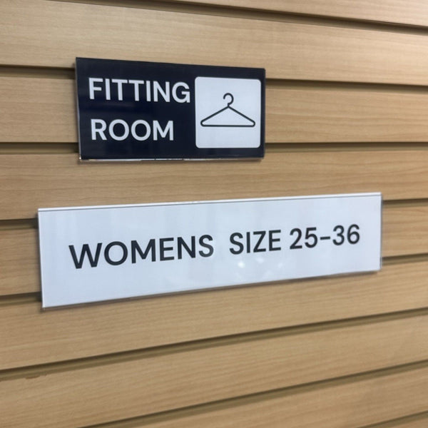 Fitting room sign with a hanger icon on a wooden wall.