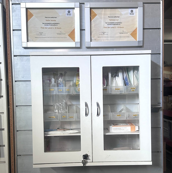 White cabinet with glass doors displaying certificates and documents on a metallic wall.