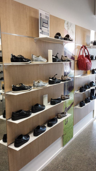 Shoe display with various shoes on wooden shelves in a store setting on custom pitch slatwall panels