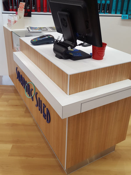 Wooden counter with electronic devices and a red cup on a white countertop.