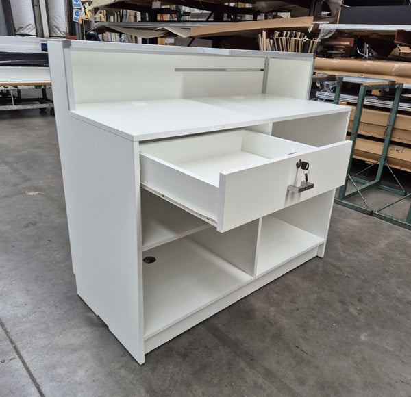 White desk with a lockable drawer in an indoor setting, possibly a warehouse or storage area.