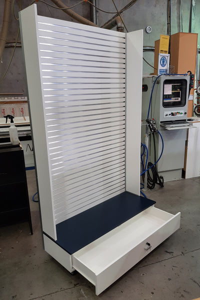 Plankwall free standing wall panel display stand in white slatwall with a black base and an open  lockable drawer in the base shown in a factory setting,