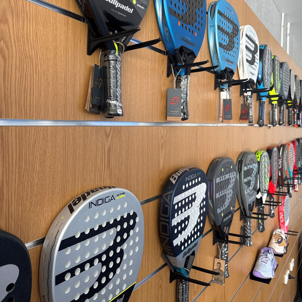 A retail display wall showcasing multiple paddle sports rackets mounted implement brackets on a  wood-grain slatwall panel background.