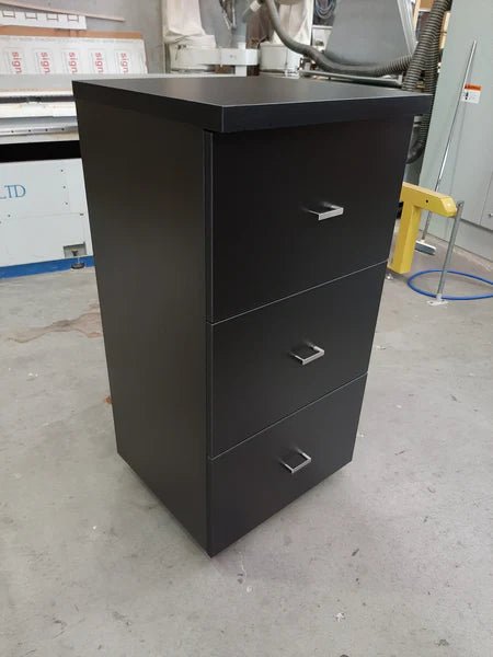 Plankwall custom three drawer cabinet in dark wood in a factory setting.