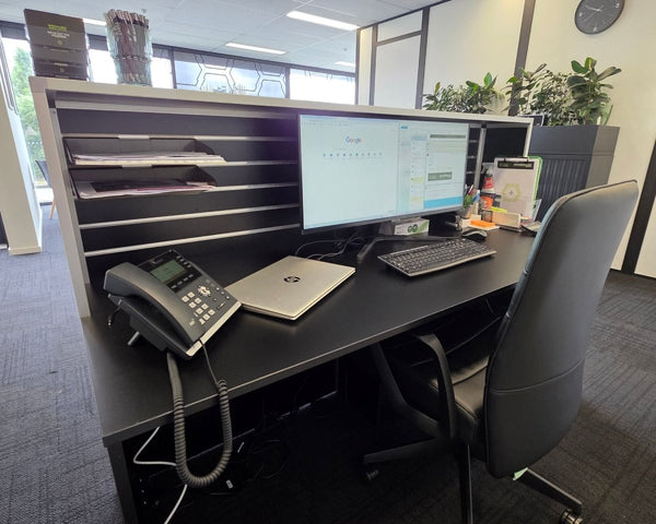 Plankwall Reception Desk with computer, phone, and chair in a room with large windows.