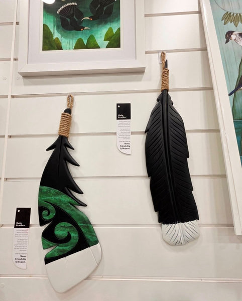 Decorative feathers with green and black patterns hung by keyhole clip on a white wall.