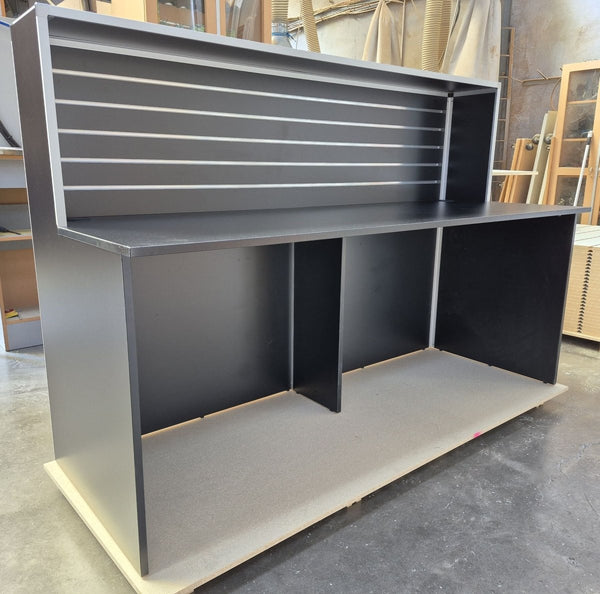 A photo of a Plankwall Reception Desk, 1800mm wide in Black shown in side view in a factory setting
