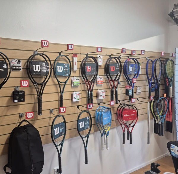 Retail slatwall with pvc inserts display of tennis rackets with Wilson branding in a store setting.