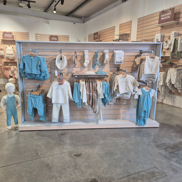 Baby clothes hung on straight arm display brackets installed on slatwall for retail merchandising.