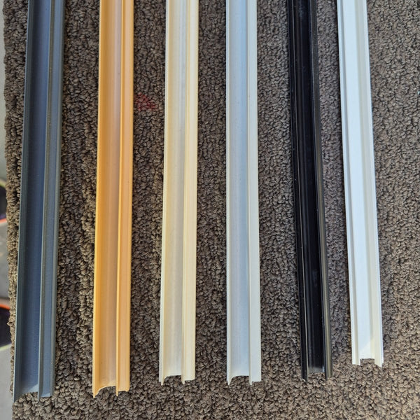 Close up of Plankwall Slatwall J inserts in a range of 6 colours, grey, tawa, cream, grey, black and white on a carpet background