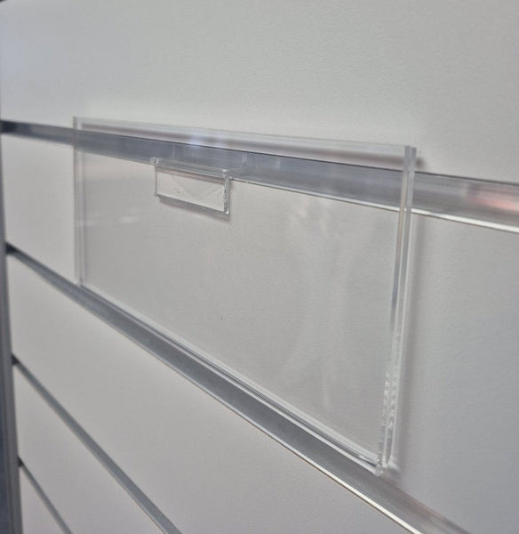 close-up of Clear acrylic slatwall header card sign holder installed on grey aluminium slatwall panel displaying retail header signage.