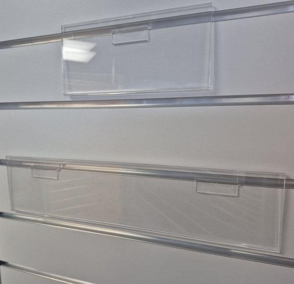 Clear acrylic slatwall header card sign holder installed on grey aluminium slatwall panel displaying retail header signage.
