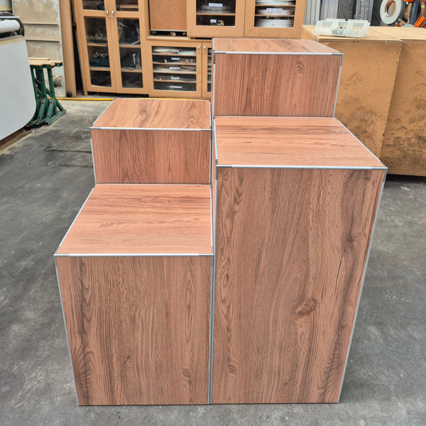 Set of 4 cube retail display stands in a woodgrain finish shown grouped together in a factory setting side view