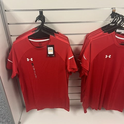 Red Under Armour shirts on hangers with a visible tag hanging on single backplate prong hooks