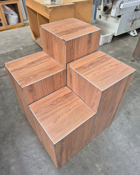 Top view of a set of 4 cube retail display stands in a woodgrain finish shown grouped together in a factory setting