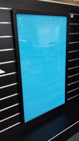 A  Plankwall aluminium snap frame powdercoated black with a clear blue tinted protective sheet, designed for displaying signs, menus, price lists and posters mounted on a black slatwall wall panel. 