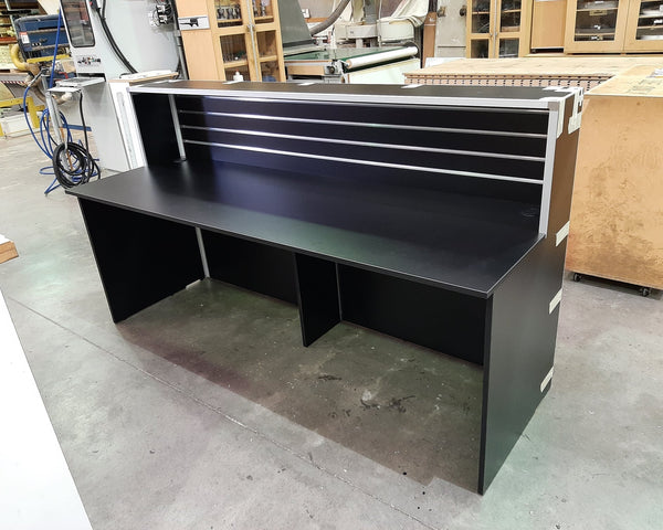Large black reception desk shown in a factory setting