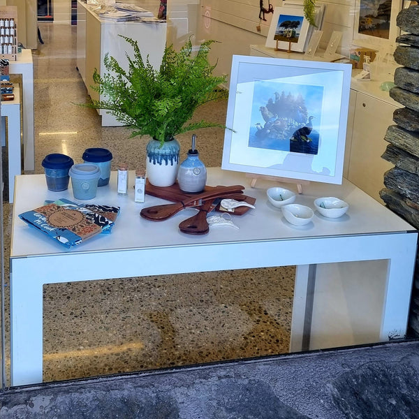 White Plankwall single nesting display table photographed through the outside window in a retail store displaying souvenirs.