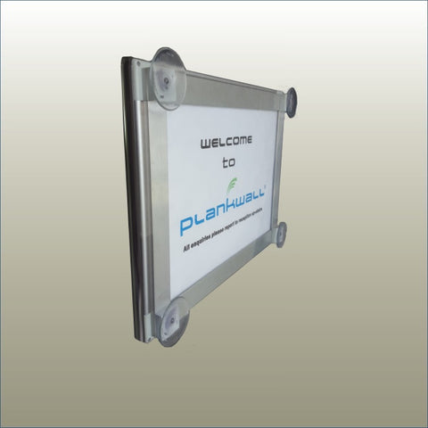 A Plankwall poster snap frame with a 'Welcome to Plankwall' sign displayed, featuring suction cups for attachment to windows.