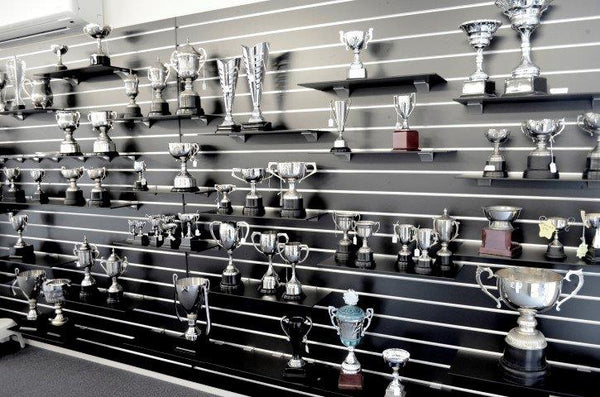 wall display of trophies mounted on black slatwall with black shelves