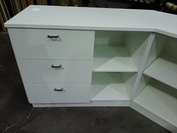 White corner cabinet with drawers and shelves on a dark floor.