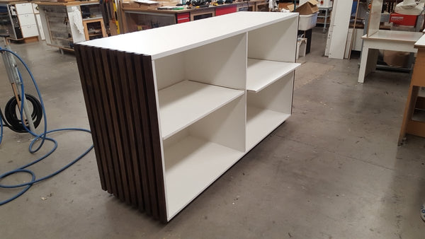 White shelves at back of a counter unit  with a slatted face in a workshop setting