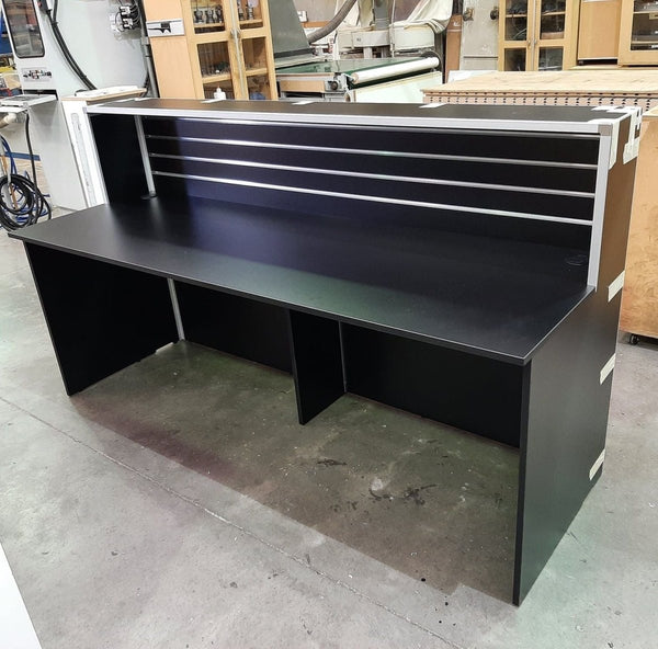 Large black reception desk shown in a factory setting