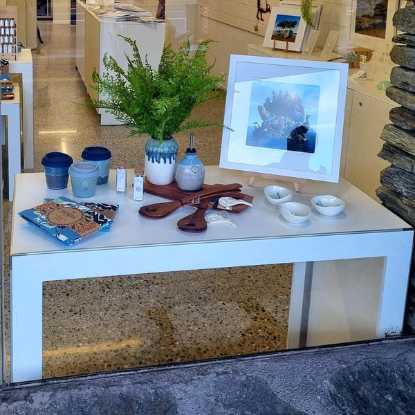 White Plankwall single nesting display table photographed through the outside window in a retail store displaying souvenirs.