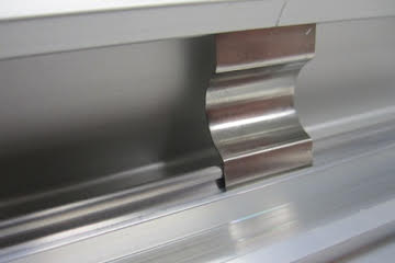 Spring clip component for hinging top and bottom poster frame extrusions, allowing smooth opening for signage replacement.
