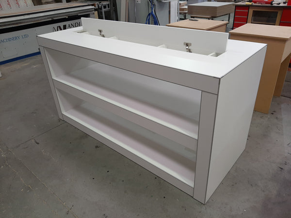 Photo of a Plankwall electronics retail display table in white showing central space for cables on hinges and shelving underneath shown in factory